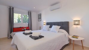 A neatly arranged hotel room with a large bed, a bedside table with books, a small side table, and a window with curtains. - Large and nice villa  with private pool in Benitachell, on the Costa Blanca, Spain for 8 persons (Benitachell)