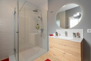 A modern bathroom with a glass shower enclosure, a wooden vanity with a white countertop, and a round mirror.