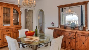 Un comedor con una mesa de vidrio, sillas blancas, un mueble de madera y una araña.
