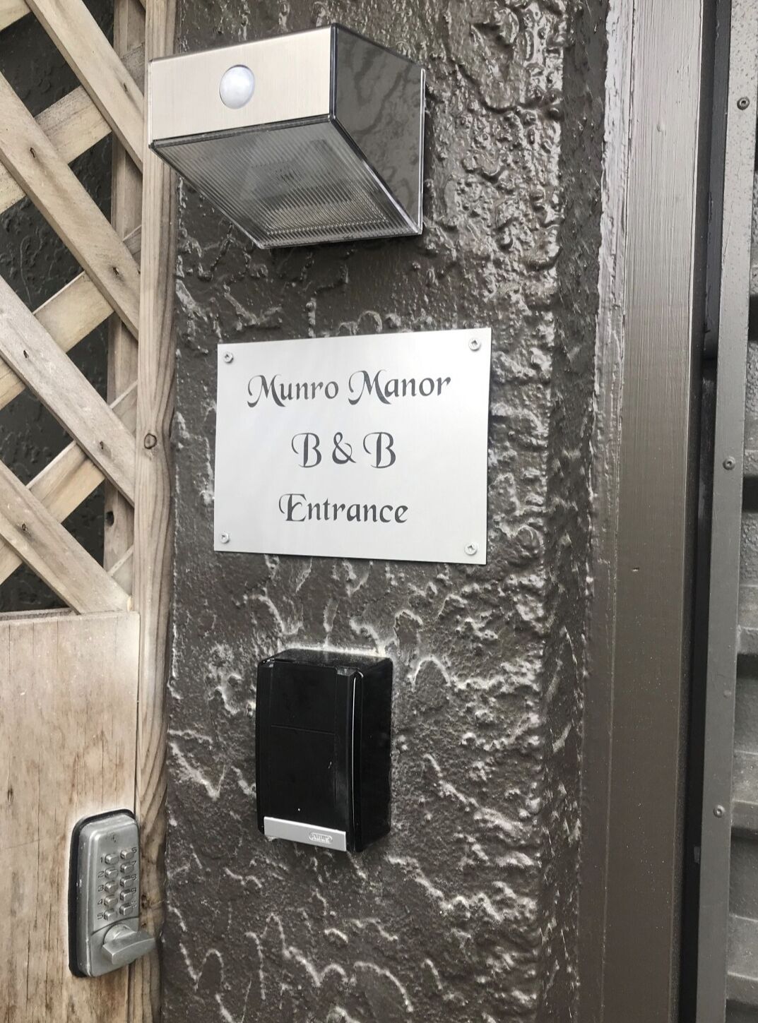 A sign for Munro Manor B&B Entrance, a keypad door lock, and a wall-mounted intercom.