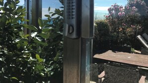 A view through a window with a metal handle and a keypad lock, overlooking a garden with bushes and a wooden deck.