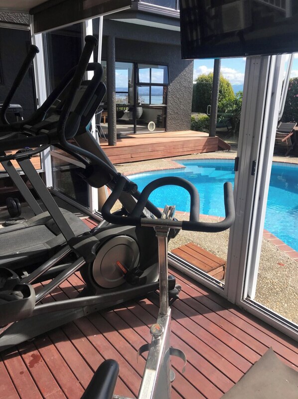 A home gym with exercise equipment, a pool, and a view of the outdoors.