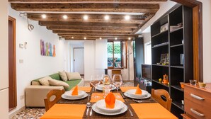 A dining area with a wooden ceiling, a table set for four with orange tablecloths, and a bookshelf to the right. - Typische venezianische Wohnung für Familien -  Venitian apartment  for families (Venice)