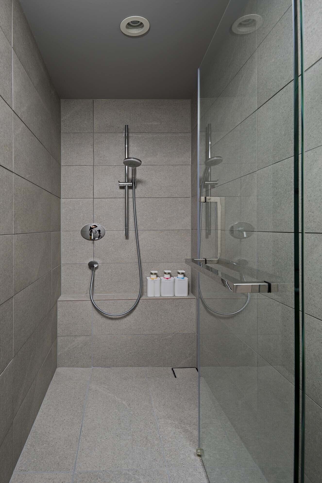 Een moderne douche met glazen douchecabine, een handdouche, een wandmengkraan en een zeepdispenser.