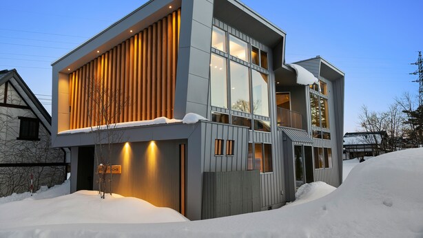 A modern two-story house with large windows and a sloped roof, surrounded by snow. - Echo Rocks (Hakuba)