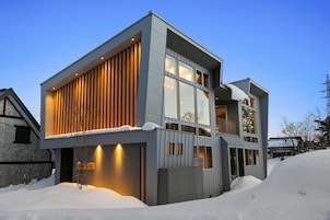 Uma casa moderna de dois andares com grandes janelas e telhado inclinado, rodeada por neve.