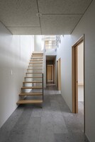Um interior moderno com uma escada que leva a um segundo andar, um corredor e uma porta à direita.