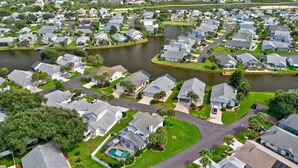 Un quartiere residenziale con case disposte attorno a un bacino d'acqua, caratterizzato da prati curati e cielo sereno.