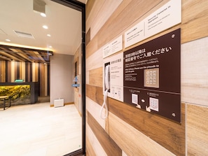 A hotel reception area with a wooden panel wall, a reception desk, and a security camera sign. - Super Hotel Iyosaijo (Saijo)