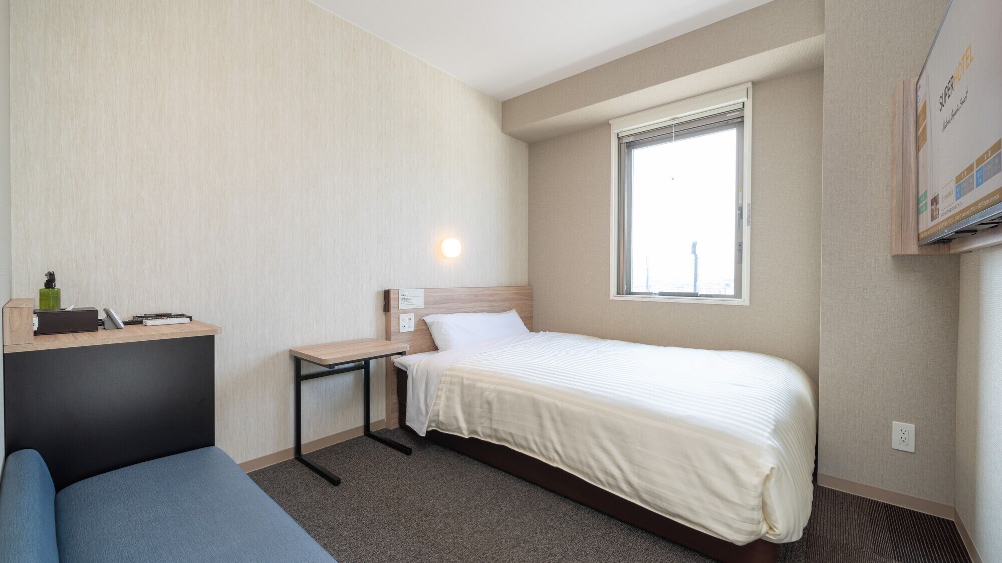 A hotel room with a bed, a desk, a chair, a window, and a wall-mounted TV.