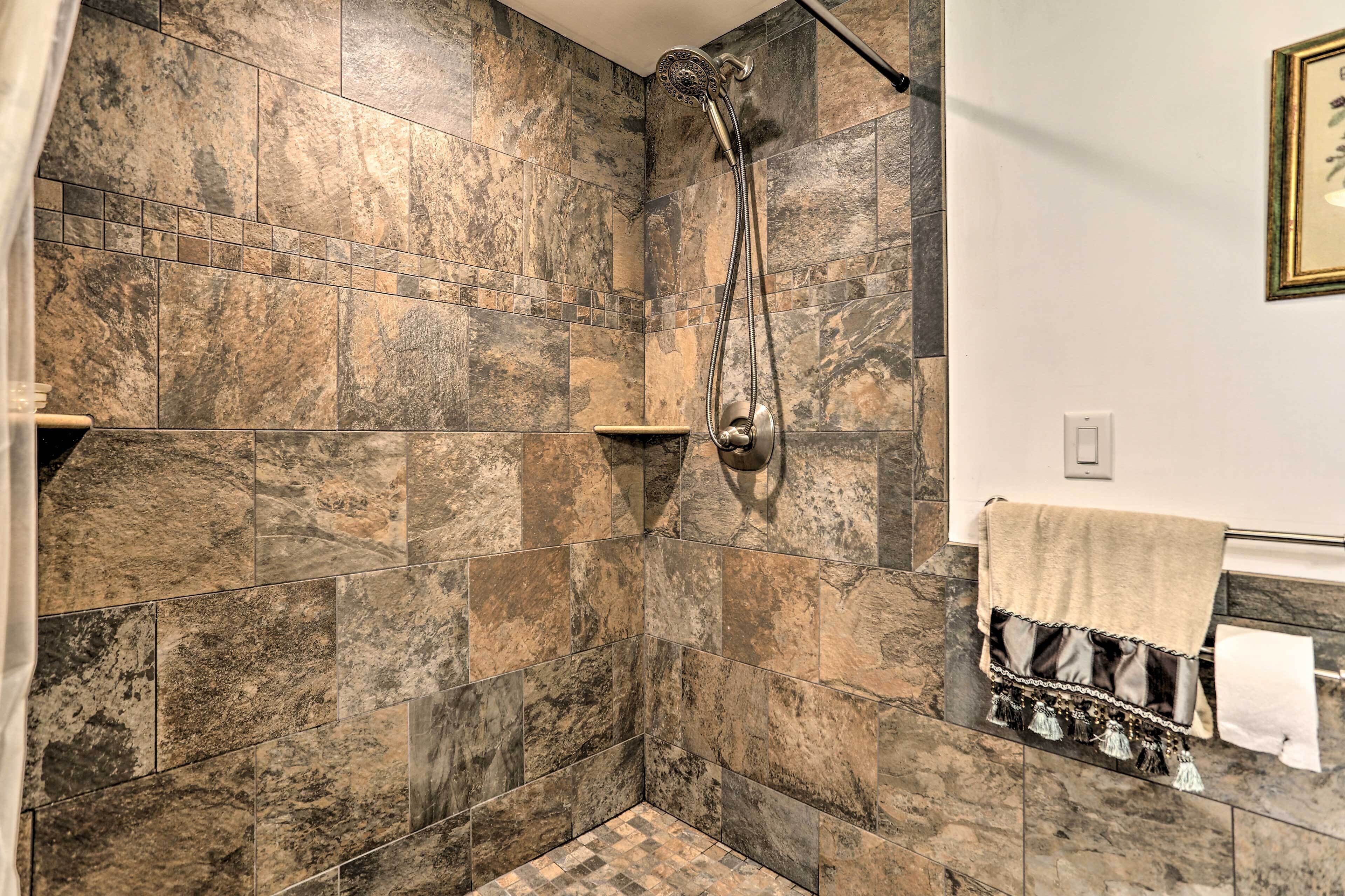 A bathroom with a shower area featuring a stone tile wall and a handheld showerhead.