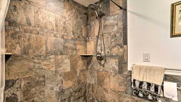 A bathroom with a shower area featuring a stone tile wall and a handheld showerhead.