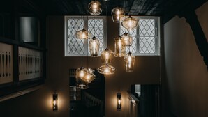 A modern interior with multiple hanging pendant lights and wall sconces, a staircase, and a window with a geometric pattern. - Hotel zum Heidkrug (Lueneburg)