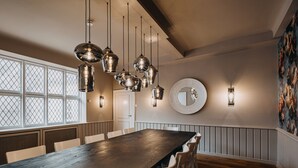A dining area with a long wooden table, hanging pendant lights, and a large round mirror on the wall. - Hotel zum Heidkrug (Lueneburg)