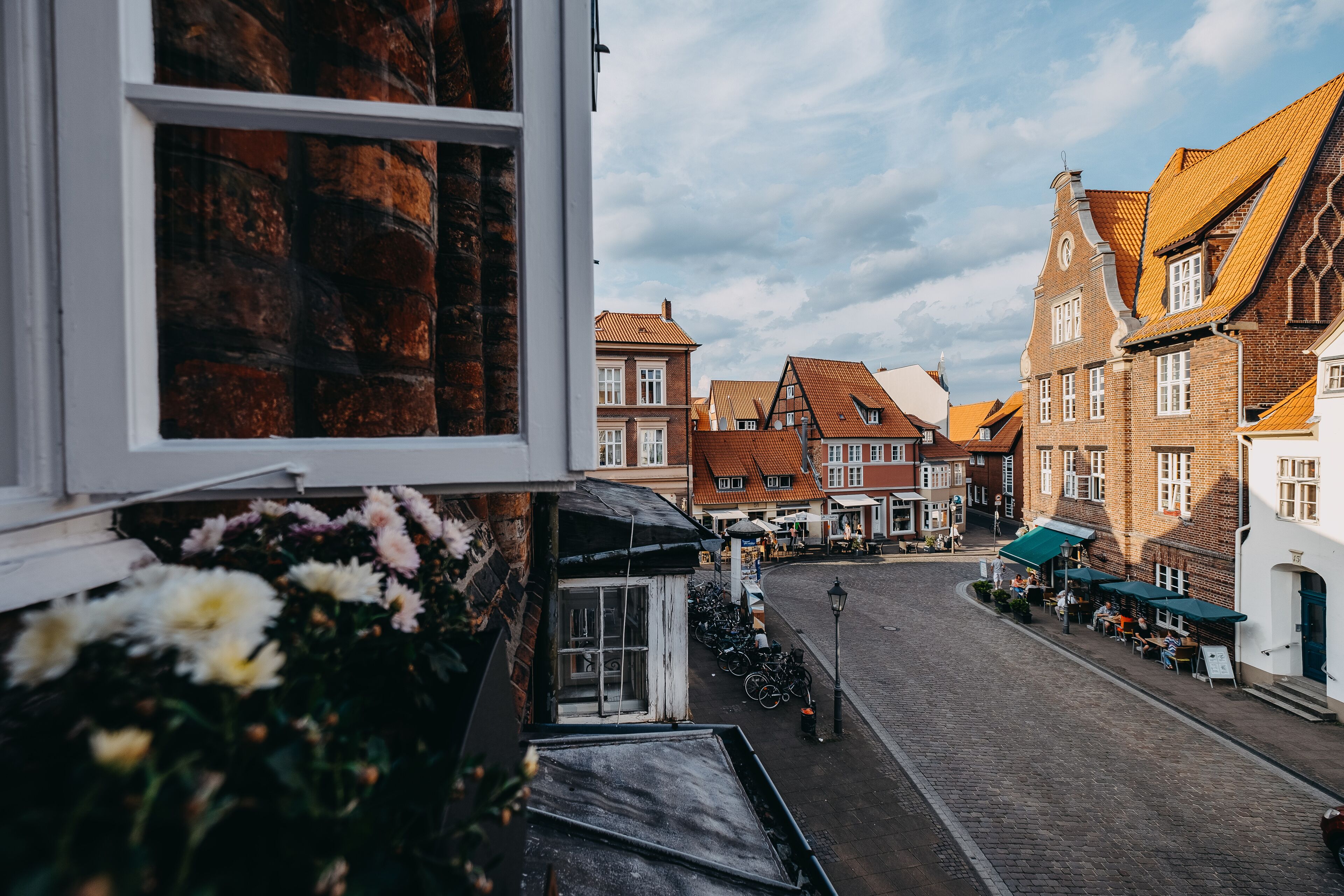Eine gepflasterte Straße gesäumt von traditionellen Backsteingebäuden, ein kleiner Laden mit einer grünen Markise und eine Blumenkiste an der Fensterbank.
