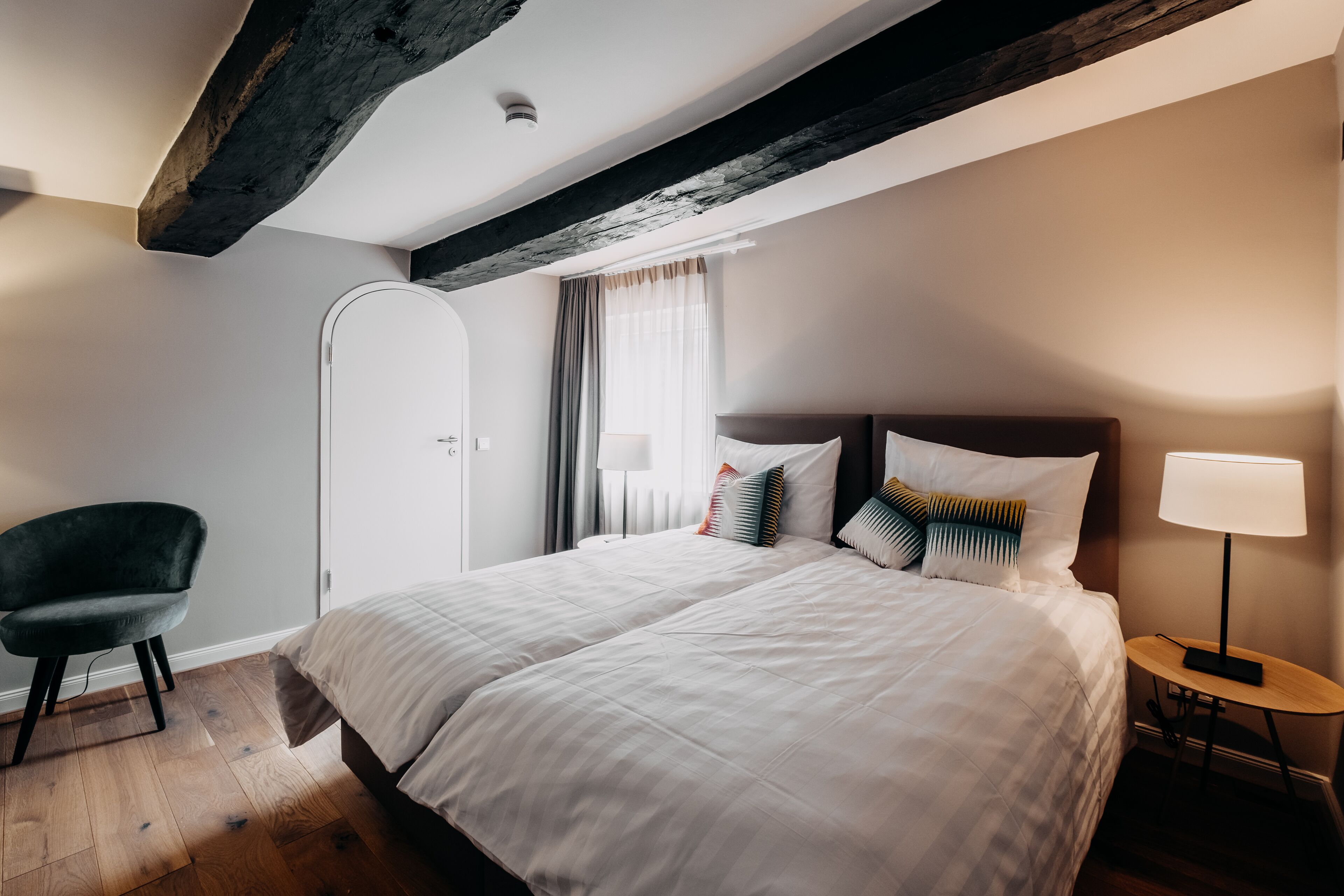 Ein Hotelzimmer mit einem großen Bett, einem Sessel, einem Nachttisch mit Lampe und einem Fenster mit Vorhängen.