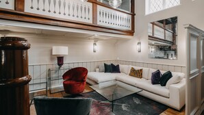 A modern living room with a sectional sofa, a glass coffee table, and a red armchair. - Hotel zum Heidkrug (Lueneburg)