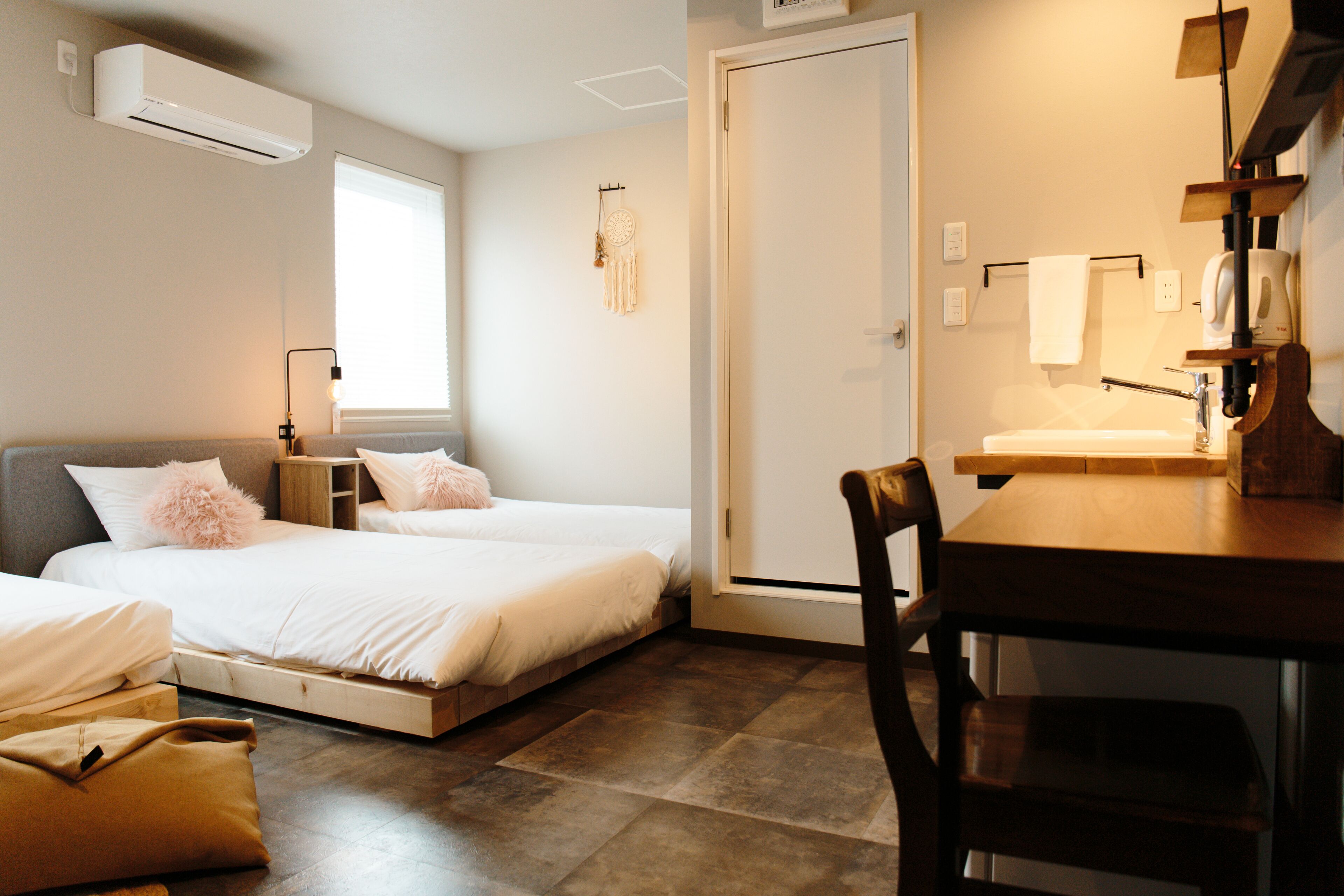 A bedroom with two beds, a wooden table, a chair, a window, and a door.