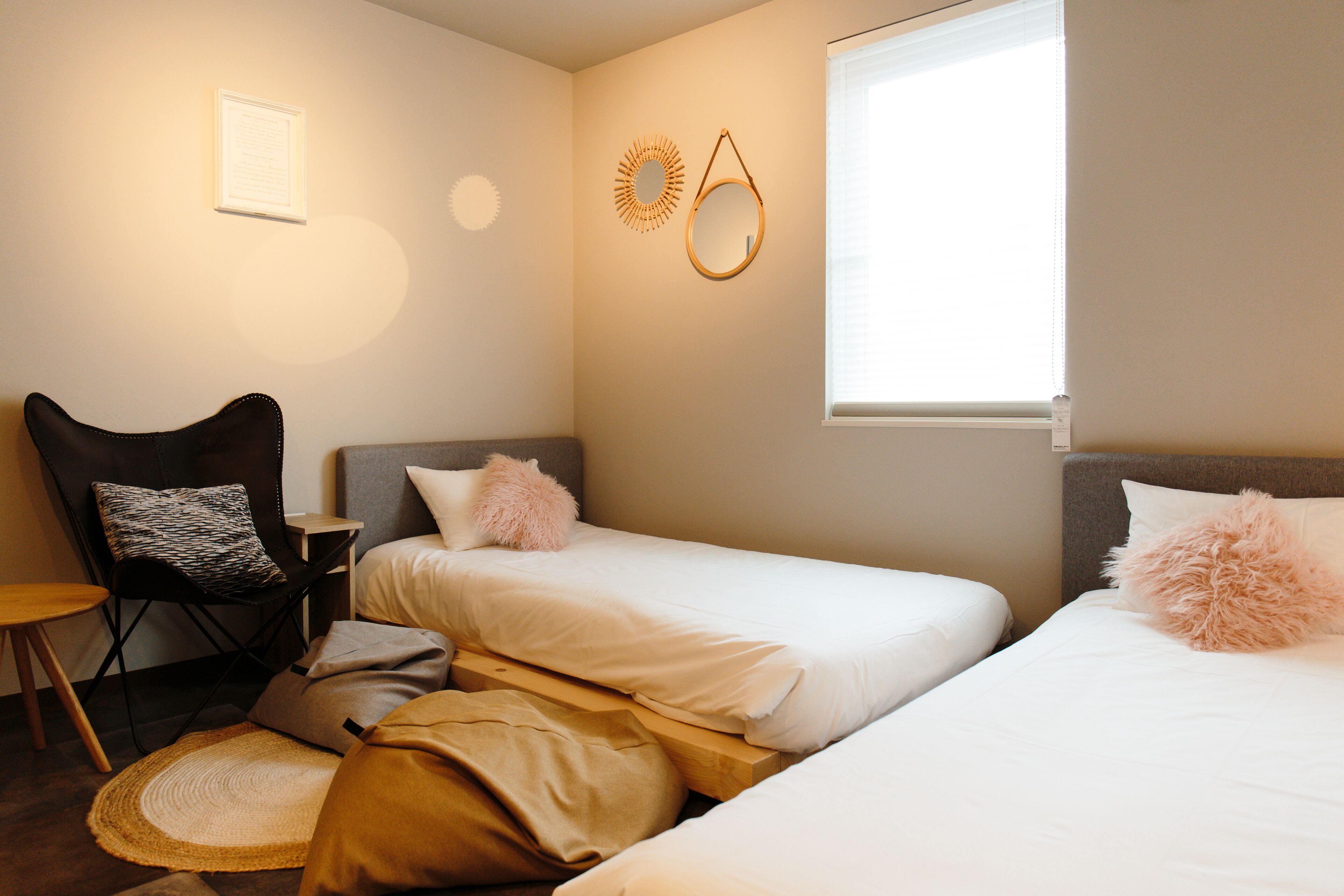 A bedroom with two single beds, a chair, a small table, and a window with blinds.