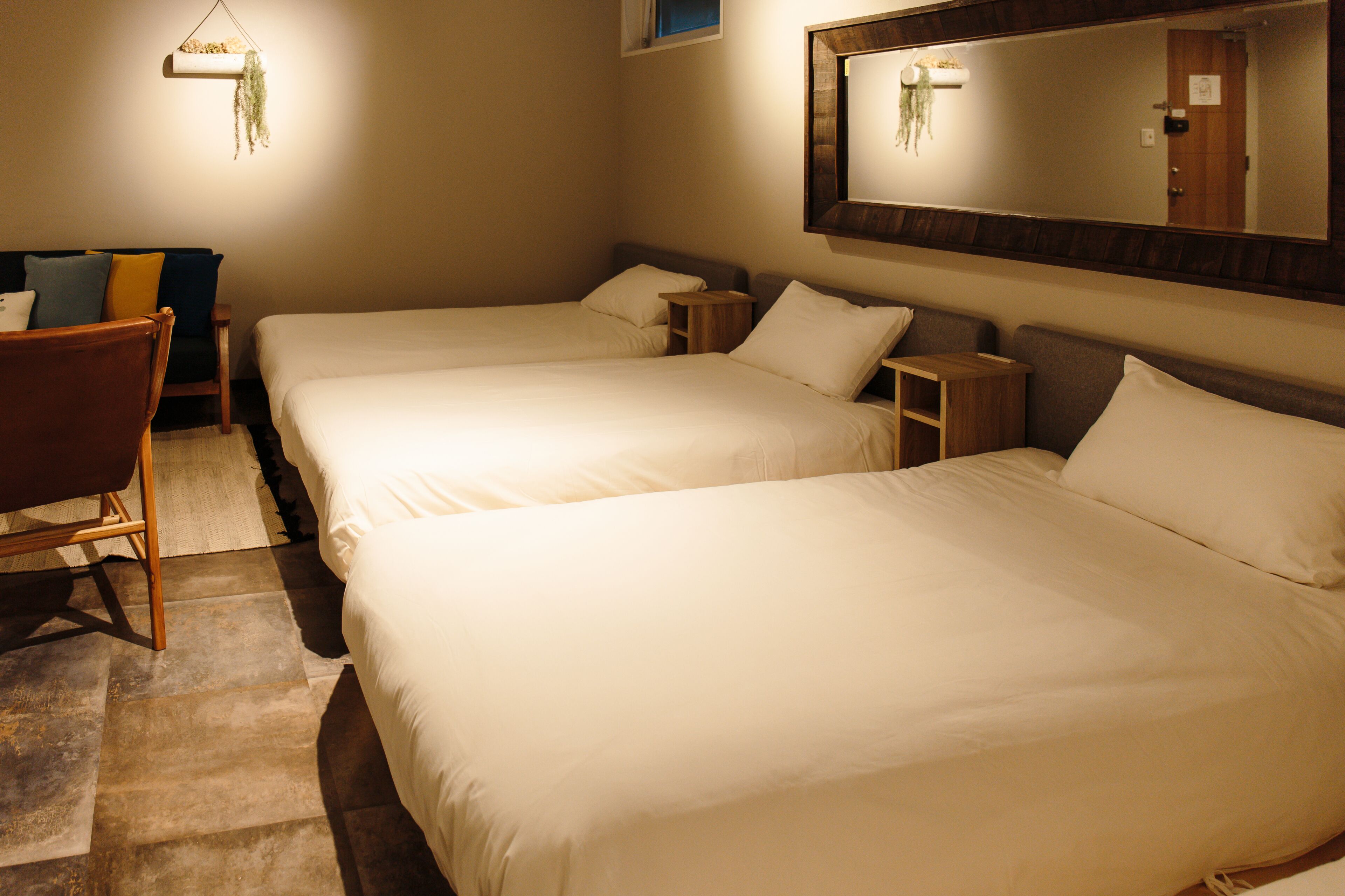 Una habitación de hotel con dos camas, una silla de madera, una mesita pequeña y una planta colgante.