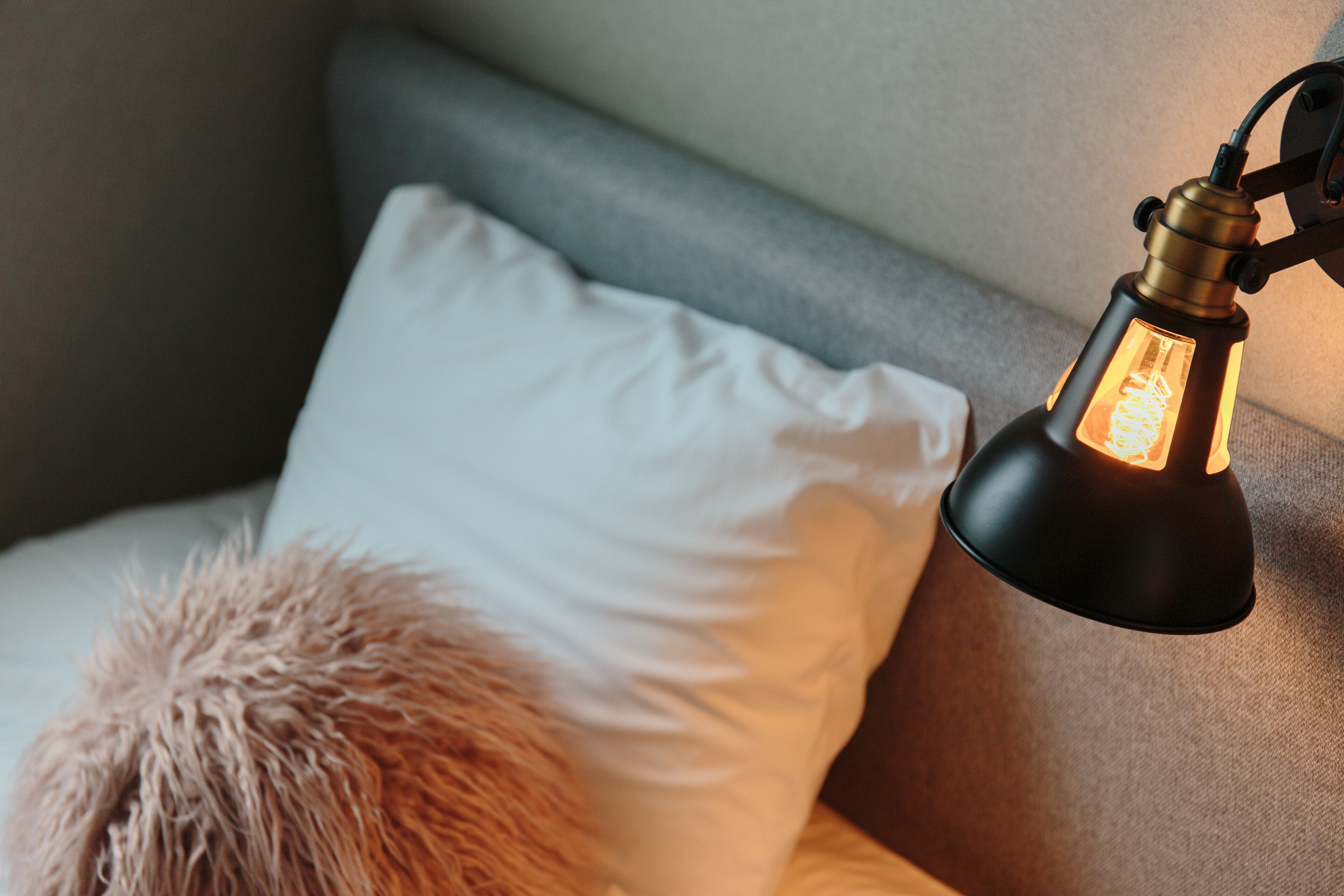 Gros plan d’un lit avec un oreiller blanc et un oreiller moelleux sur le côté.
