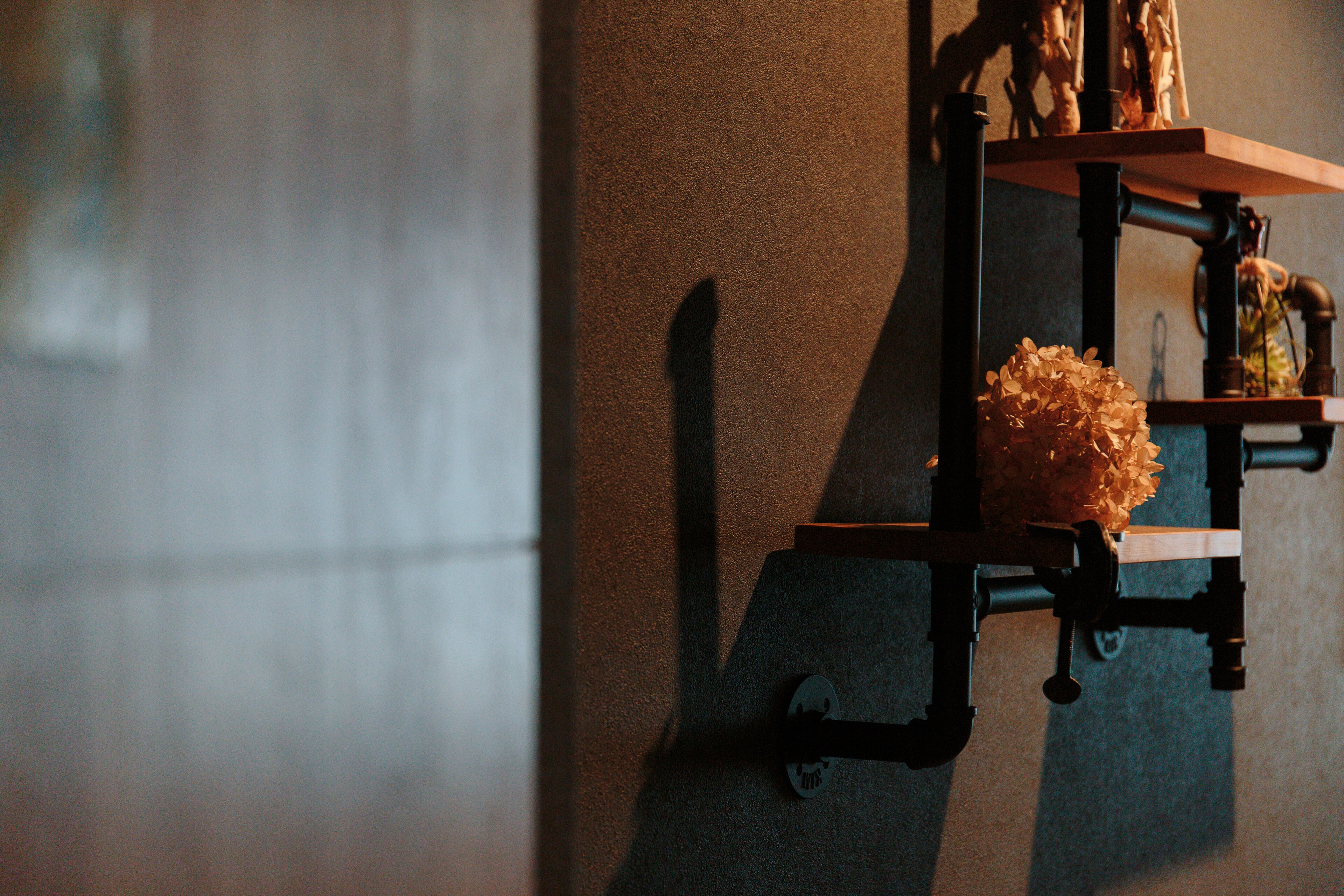 Une étagère fixée au mur, ornée d’un vase de fleurs, d’une petite statue et d’une pipe.