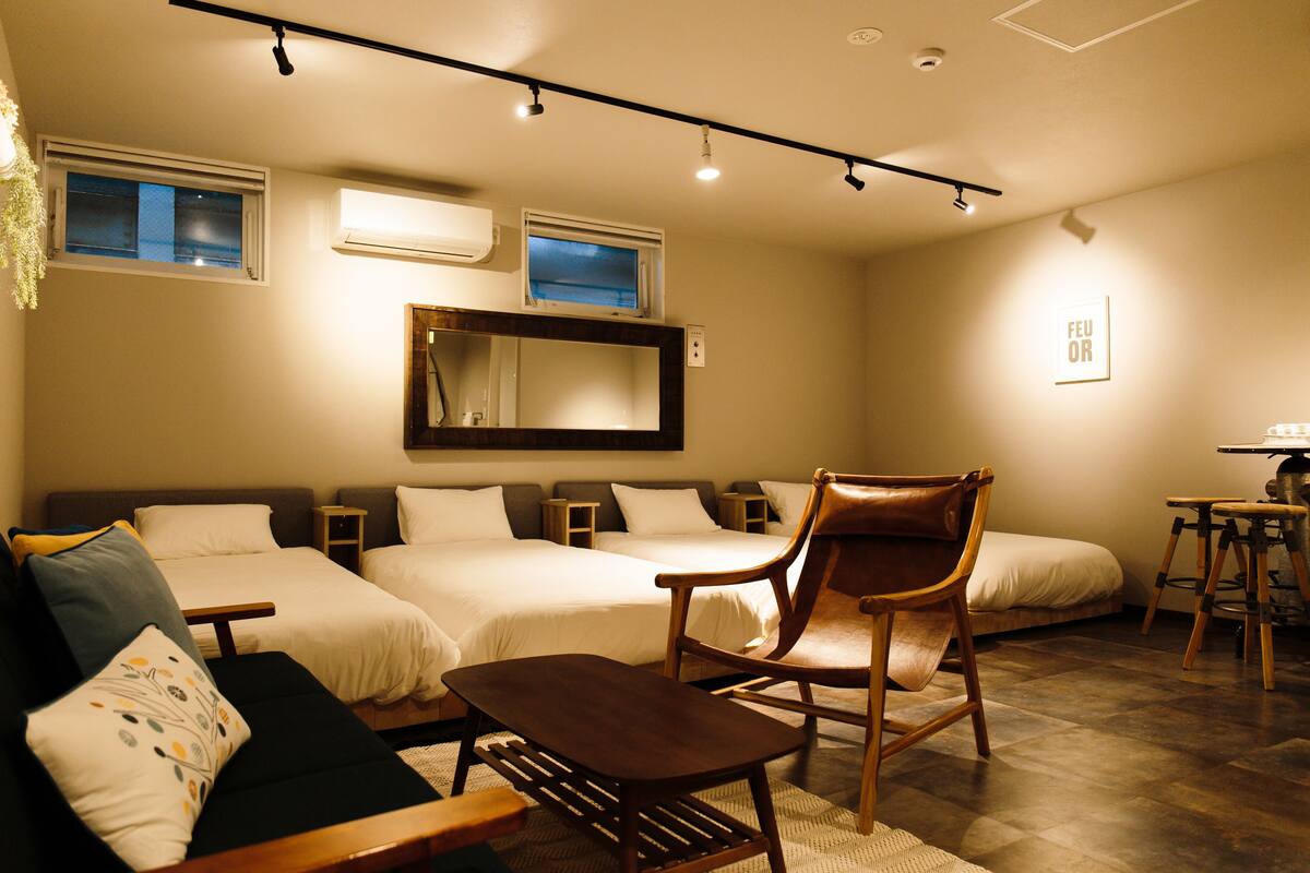 Quarto de hotel com duas camas, um sofá, uma cadeira e uma mesinha.