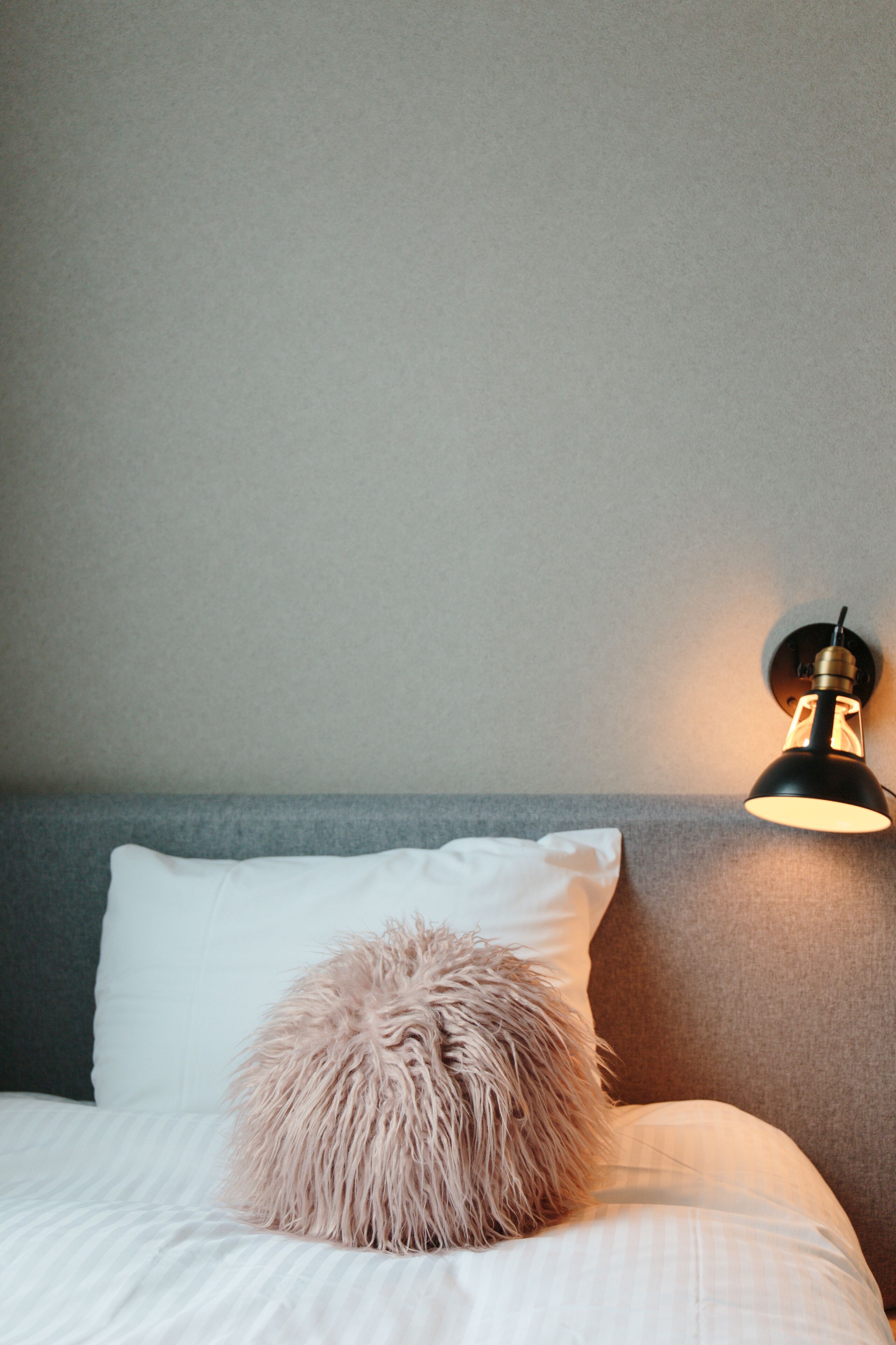 Una cama bien tendida con un almohadón mullido y una lámpara de pared.