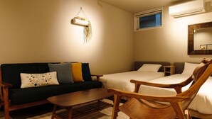 Ein gemütliches Zimmer mit einem dunkelgrünen Sofa, einem Holzstuhl, einem kleinen Tisch und zwei Einzelbetten.