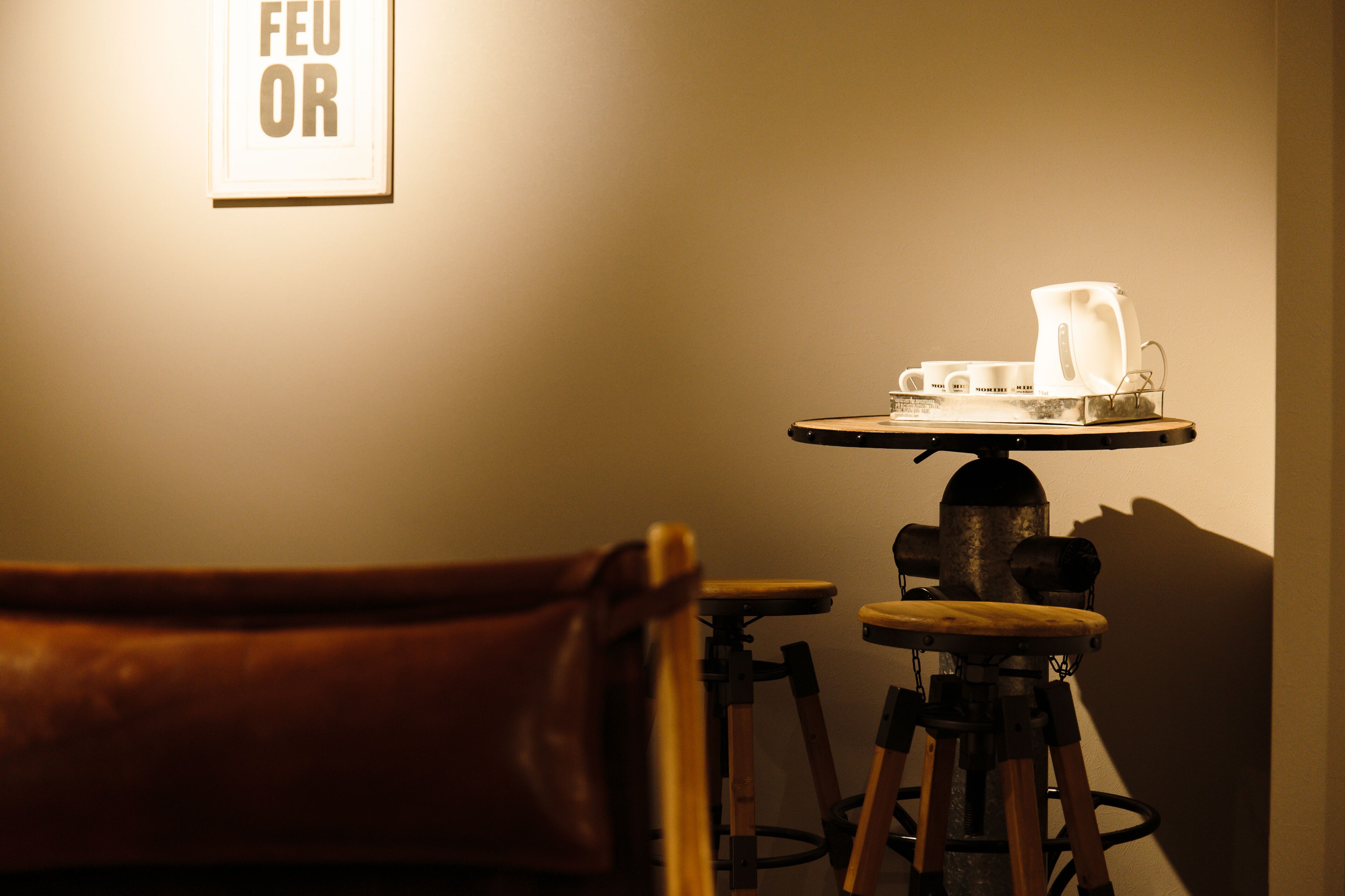 A table with a coffee pot and cups, a chair, and a wall-mounted sign.