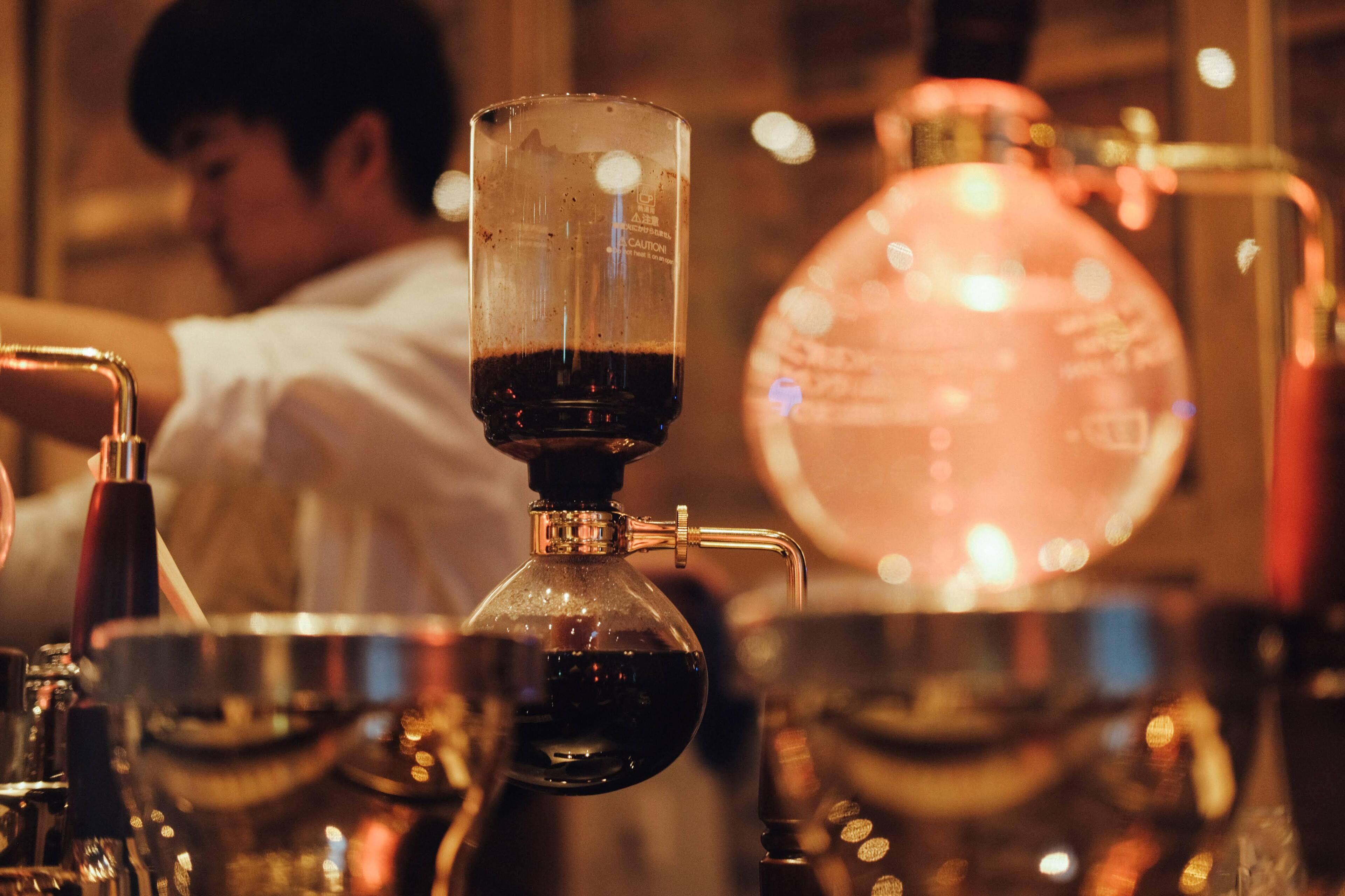 A coffee machine with a clear glass container and a spout, a large spherical glass container, and a metal bowl.