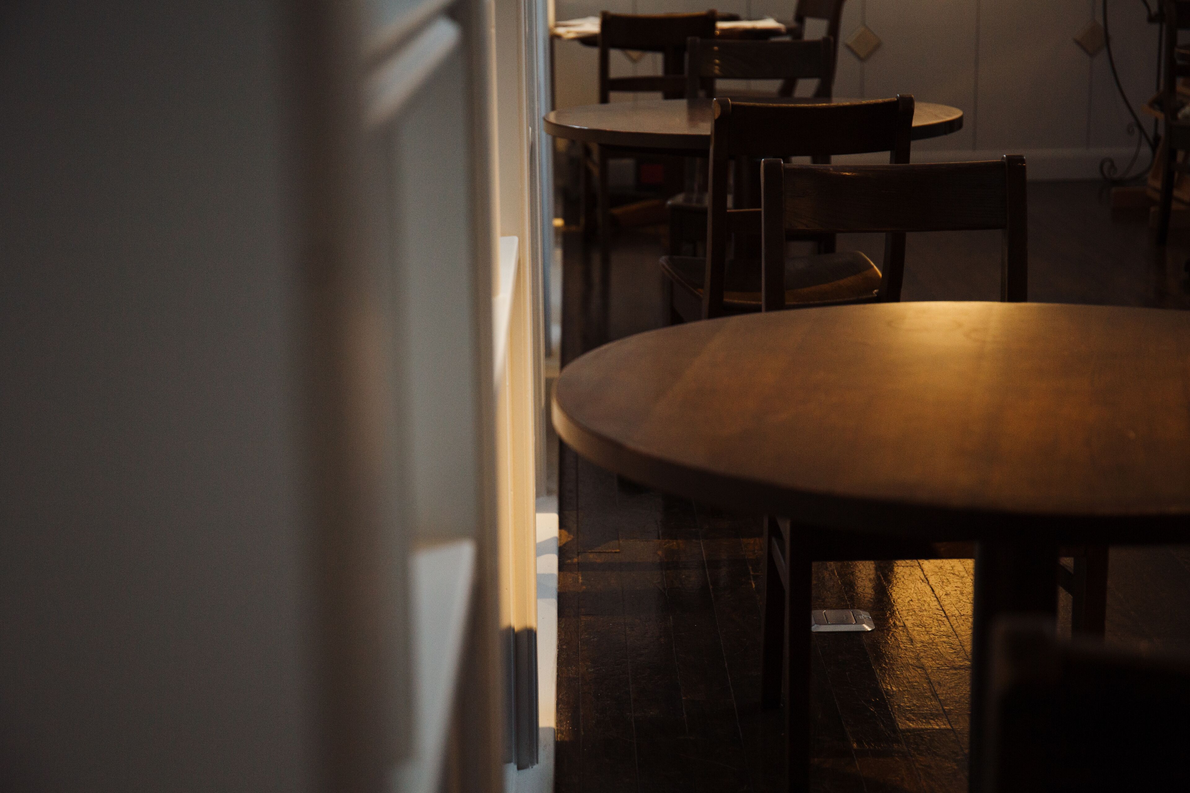 A dimly lit room with a wooden table and chairs, a door, and a tiled floor.