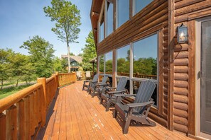 A wooden deck with Adirondack chairs and a view of a green landscape.