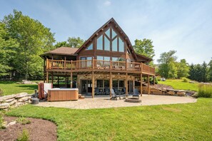 A two-story log cabin with a balcony, outdoor seating, and a hot tub.