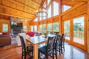A spacious wooden cabin with a dining area, fireplace, and large windows.