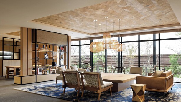 Un interior moderno con una gran mesa de comedor, sillas y un sofá. Se ve una estantería y una ventana con vistas al exterior.