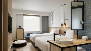 Una habitación de hotel moderna con dos camas, un ventanal con cortinas, suelo de madera, un lavamanos redondo y un espejo con marco negro.