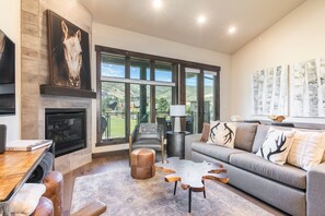 A modern living room with a fireplace, large windows, a sofa, and a coffee table.