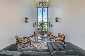 A modern interior with a high ceiling, a large window offering a view of a landscape, and a seating area with leather sofas and chairs.
