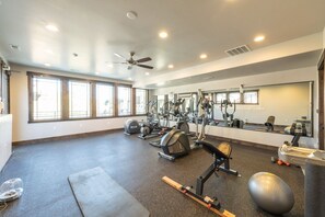 Una palestra con diverse attrezzature per esercizi, ampie finestre e una ventola a soffitto.