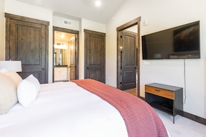 Une chambre d’hôtel avec un grand lit, un téléviseur fixé au mur, un bureau et des portes en bois.