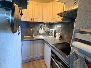 A compact kitchen with wooden cabinets, a stainless steel sink, a coffee maker, and a kettle.