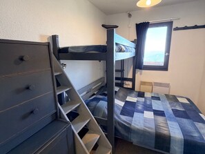 A bunk bed room with a dresser, a window with curtains, and a radiator.