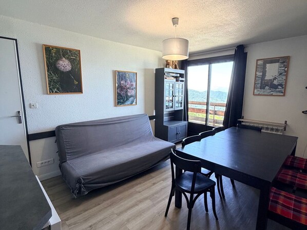 A compact living space with a sofa, dining table, chairs, a cabinet, and artwork on the walls.
