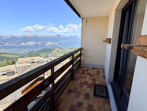A balcony with a wooden railing, a tiled floor, and a view of mountains and valleys.