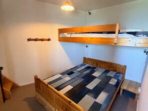 Ein Einzelbett mit karierter Matratze, darüber ein Stockbett und eine kleine Tischrechnung rechts.