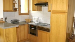 A compact kitchen with wooden cabinets, a built-in oven, a dishwasher, and a window. - High-end 4-room duplex at the foot of the slopes with parking (Les Adrets-Prapoutel)