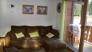 A living room with a brown sofa, two cushions, a wooden coffee table, and a sliding glass door leading outside. - High-end 4-room duplex at the foot of the slopes with parking (Les Adrets-Prapoutel)