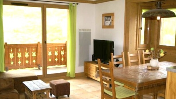 A dining area with a wooden table, chairs, and a bench. There is a television on a stand, a window with curtains, and a picture on the wall. - High-end 4-room duplex at the foot of the slopes with parking (Les Adrets-Prapoutel)