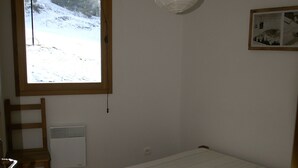 A bedroom with a wooden bed, a window with a view of a snowy landscape, a radiator, and a wooden chair. - High-end 4-room duplex at the foot of the slopes with parking (Les Adrets-Prapoutel)